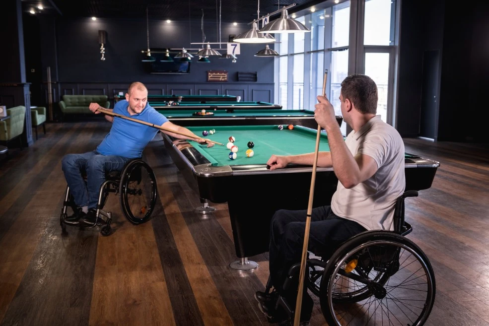 Two disabled friends in wheelchairs playing a game of pool at a local pub