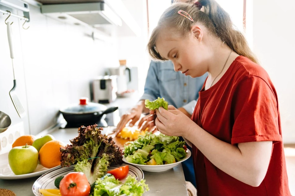 Disabled girl learning how to make a salad at home with carer