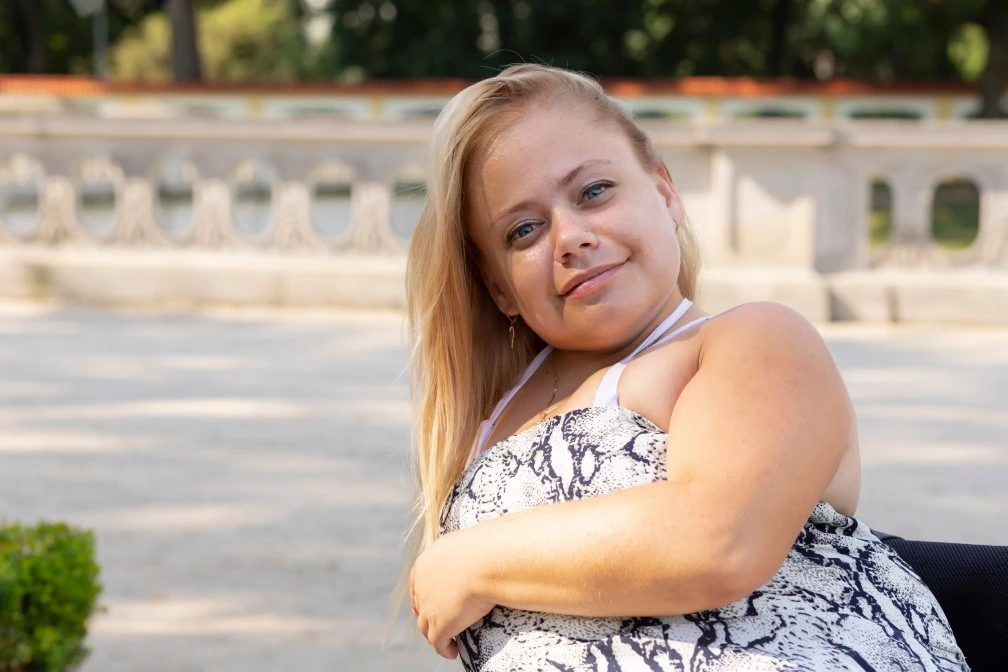 Beautiful blonde disabled woman sitting outside in wheelchair and smiling at camera