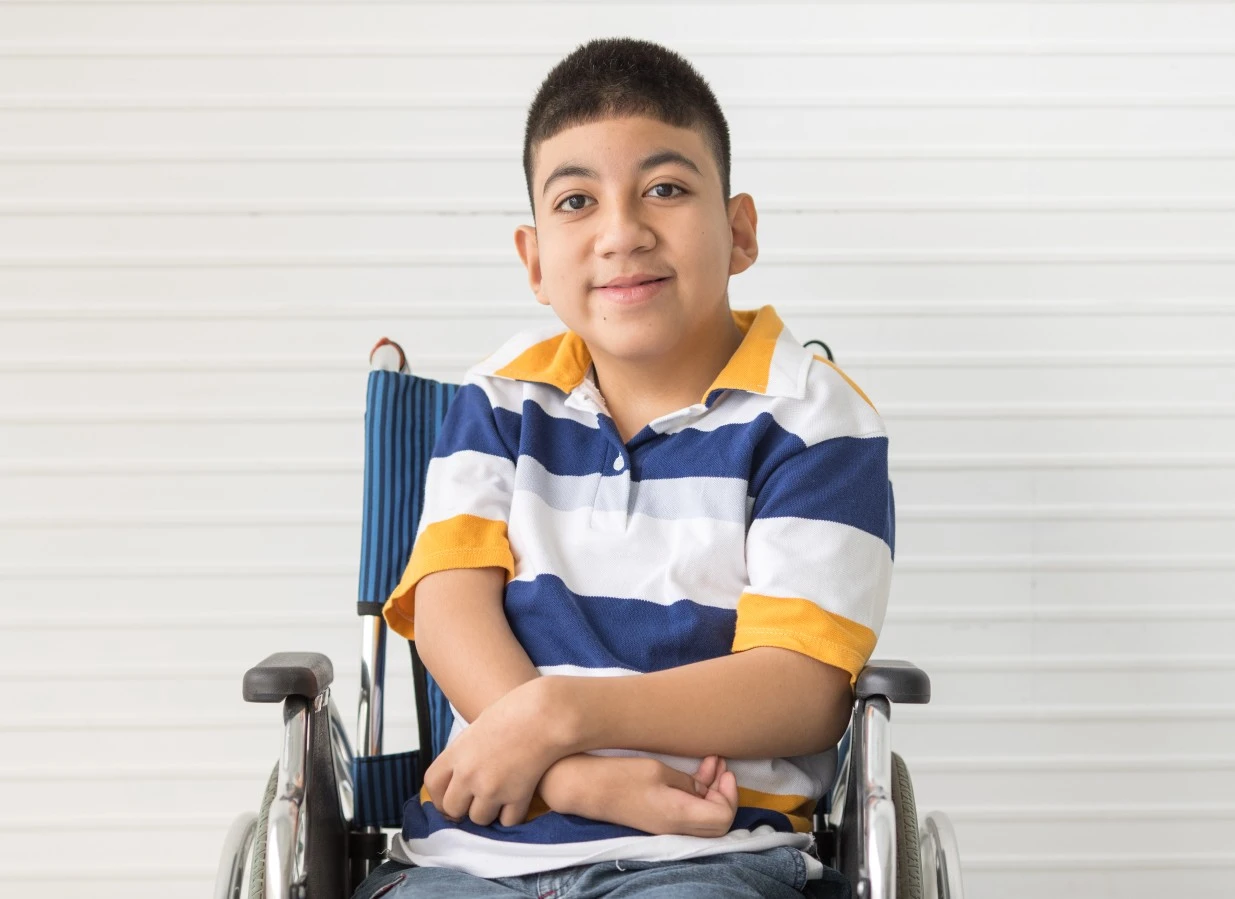 Disabled boy sitting in wheelchair with arms crossed smiling at camera
