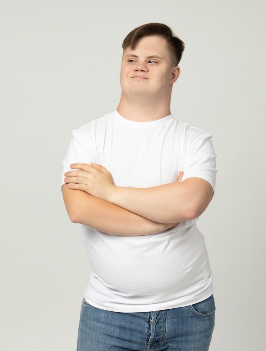 Smiling young man with down syndrome in jeans and white t-shirt posing in front of the camera